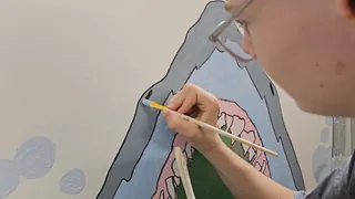 Eine Schülerin malt mit einem Pinsel ein großes Wandbild.