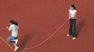 Zwei Schülerinnen beim Seilspringen auf dem roten Sportplatz.