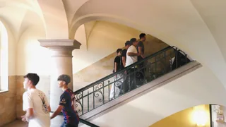 Schüler begegnen sich auf einer Treppe unter hellen Gewölben.