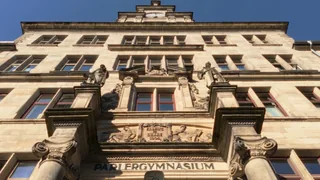 Blick nach oben auf die symmetrische Sandsteinfassade des Parler-Gymnasiums.