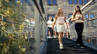 Eine Gruppe geht im Sonnenlicht über die Glasbrücke.