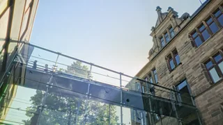 Blick von unten auf die gläserne Brücke und den historischen Altbau.