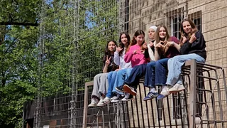 Eine Gruppe Schülerinnen sitzt zusammen an einem Geländer vor Bäumen und einer Mauer.